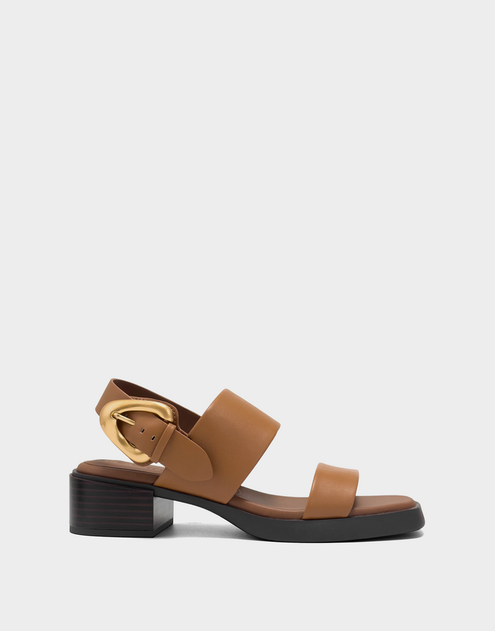 A tan leather block-heel sandal with a gold buckle and a black sole, shown from a side profile on a light gray background.