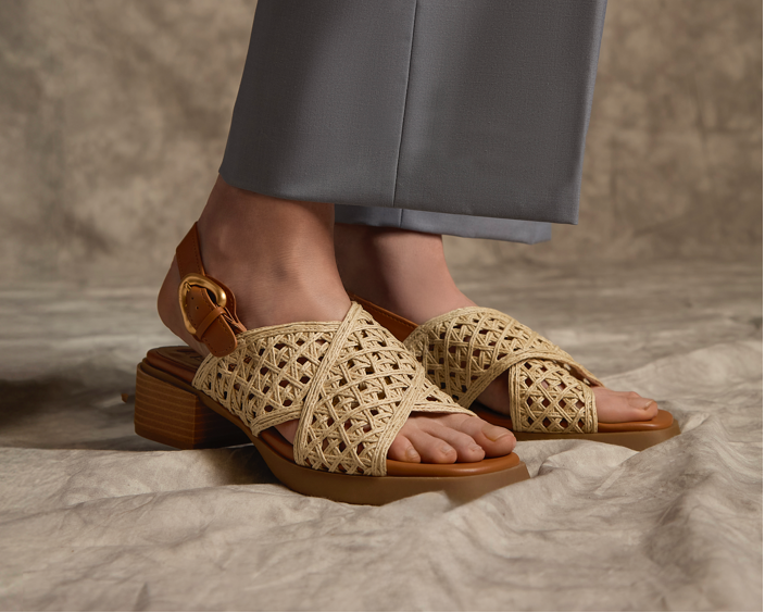 Beige woven sandals worn with gray pants on a textured surface