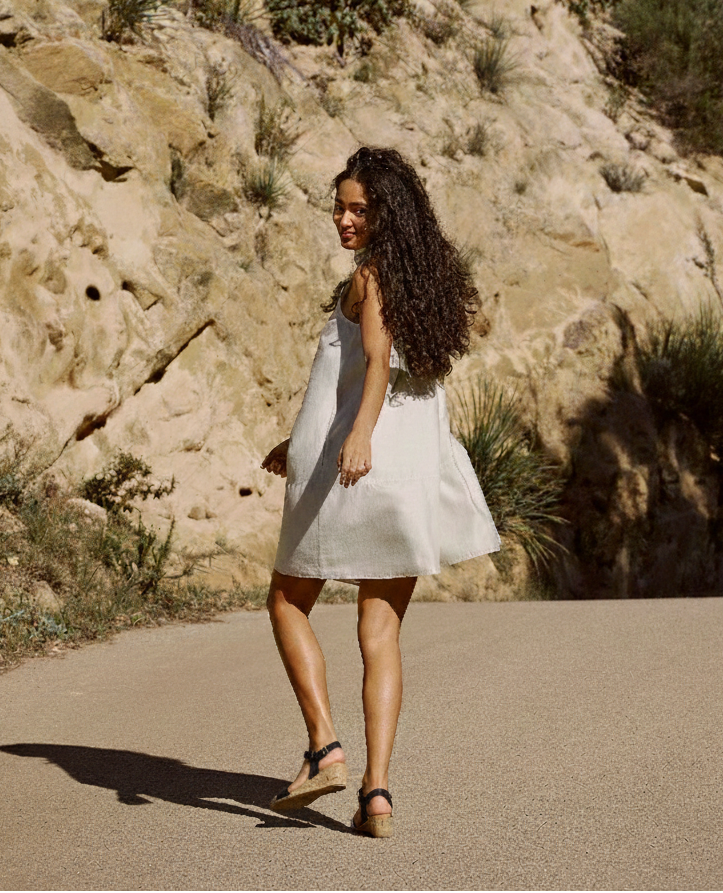Woman walking outdoors in a light summer dress wearing Aerosoles WEL black cork wedge sandals, featuring an adjustable ankle strap and cushioned sole, styled for comfortable warm-weather wear.