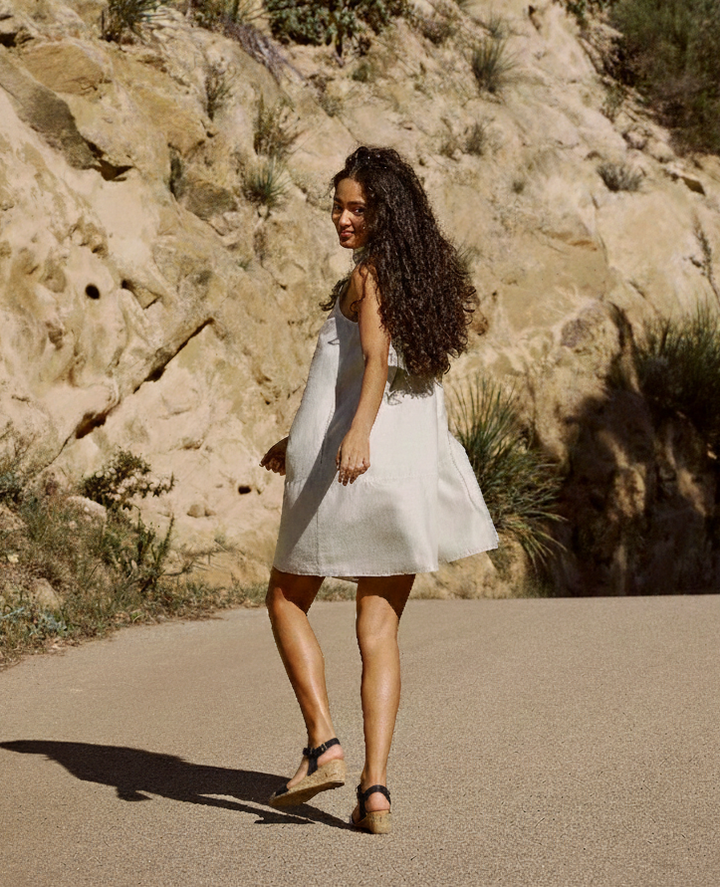 Woman walking outdoors in a light summer dress wearing Aerosoles WEL black cork wedge sandals, featuring an adjustable ankle strap and cushioned sole, styled for comfortable warm-weather wear.